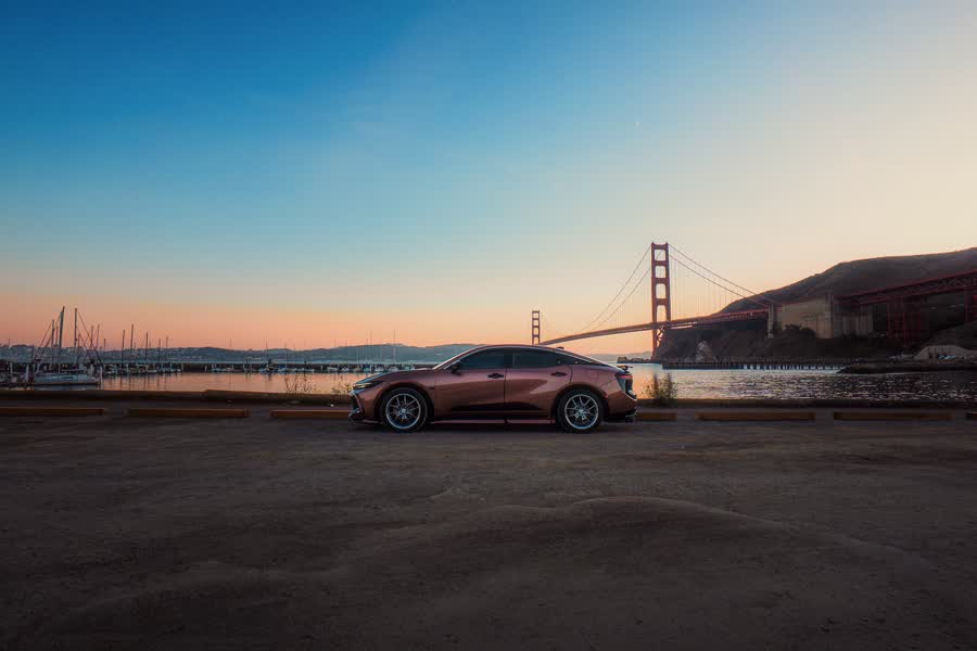 A sedan parked on gravel with the Golden Gate Bridge behind it at dusk