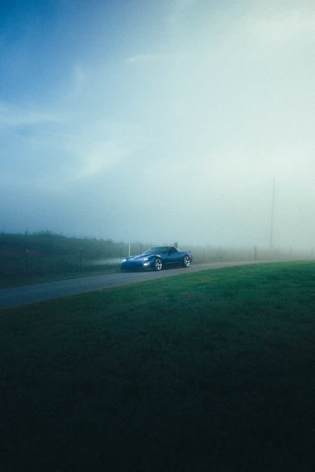 A blue sports car emerging from thick fog on a country road