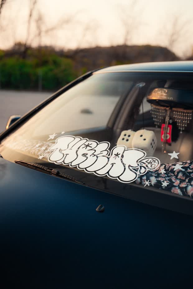 Close detail of a windscreen with a graffiti-style decal and fluffy dice hanging from the mirror